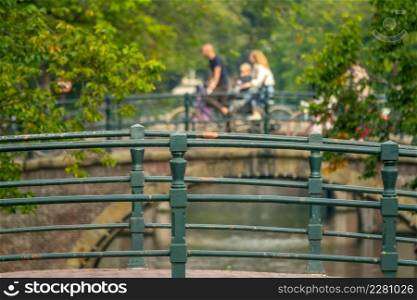 Netherlands. Bridges over a canal in Amsterdam surrounded by green trees. Defocused family on bikes. Bridges over the Amsterdam Canal and Family on Bikes