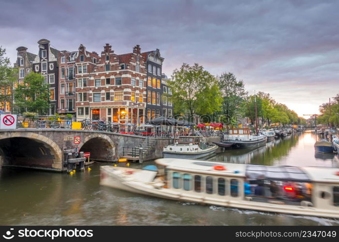 Netherlands. Cloudy twilight on the canal of Amsterdam. Houseboats and boats are moored. Reflection in the water of traditional houses and a bridge. Amsterdam Canal at Cloudy Twilight