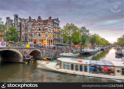 Netherlands. Cloudy twilight on the canal of Amsterdam. Houseboats and boats are moored. Reflection in the water of traditional houses and a bridge. Amsterdam Canal at Cloudy Twilight