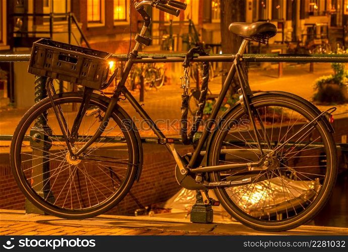 Netherlands. Night Amsterdam. Bicycle with a luggage basket is parked at the canal fence and secured with an anti-theft chain. Parked Bicycle in Amsterdam at Night