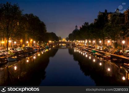 Netherlands. Night Amsterdam. Lanterns and parked cars on the embankments. Many boats are moored along the banks of the canal. Night Canal in Amsterdam With Parked Cars and Boats