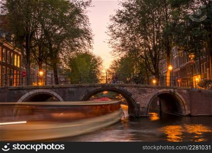 Netherlands. Quiet sunset on the Amsterdam Canal. Pleasure boat under the stone bridge. Sunset on the Amsterdam Canal and a Boat Under the Bridge