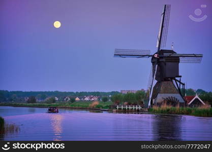 Netherlands rural landscape with windmills at famous tourist site Kinderdijk in Holland in twilight with full moon and boat in canal. Windmills at Kinderdijk in Holland. Netherlands