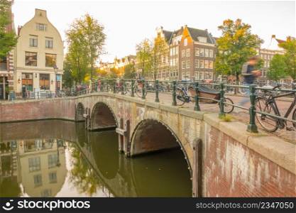 Netherlands. Stone bridge with three arches on the Amsterdam canal. Lots of parked bikes. Morning with the first rays of the sun. Morning on the Amsterdam Bridge