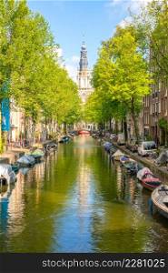 Netherlands. Sunny summer day on the Amsterdam canal. Parked cars on the embankment and many moored boats on the water. Cathedral building in the distance. Amsterdam Canal with Boats on a Sunny Day