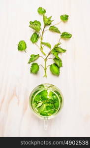 Nettle and glass tea pot on white wooden background, top view