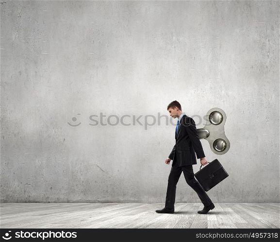 Never endless energy. Young businessman walking with wind up key in his back