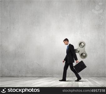 Never endless energy. Young businessman walking with wind up key in his back