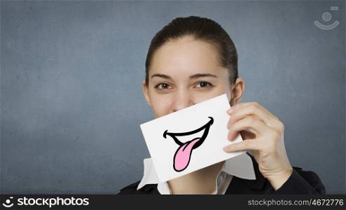 Never stop smiling. Pretty young girl holding white card with drawn smile showing tongue