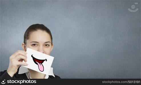 Never stop smiling. Pretty young girl holding white card with drawn smile showing tongue