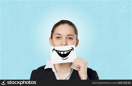 Never stop smiling. Pretty young girl holding white card with drawn smile with teeth