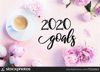 New 2020 year plan with beautiful fresh pink and white peony flowers on pink table with cup of coffee, frame with copy space for your text, top view and flat lay background. Fresh peony flowers