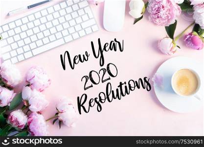 New 2020 year resolutions modern keyboard with female accessories and fresh peony flowers, copy space on pink background. Top view home office workspace