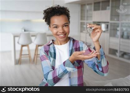 New apartment buyer. Happy teenager is homeowner in living room of new residence. Carefree african american girl is holding house key and smiling. Mortgage loan and relocation conceptual image.. Carefree african american girl is holding house key and smiling. Happy teenager is homeowner.