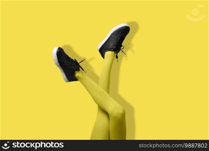 New Black female sneakers on long slender woman legs in yellow tights isolated on yellow background. Monochrome pop art concept.. New Black female sneakers on long slender woman legs in yellow tights isolated on yellow background