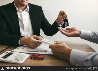 New car buyers and car sales agent people are exchanging by giving cash and new car keys to each other in the office.