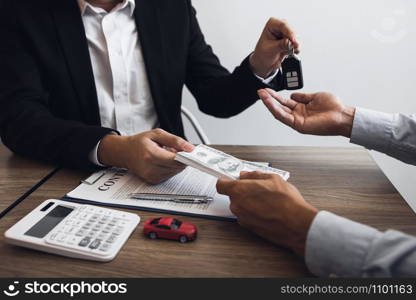 New car buyers and car sales agent people are exchanging by giving cash and new car keys to each other in the office.