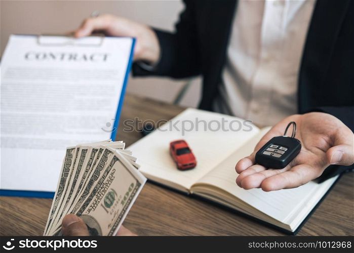 New car buyers are holding cash and handing it to car salespeople while filing a new car signing contract for car buyers.