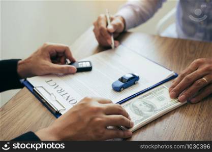 New car buyers are signing a contract with a car salesman at the showroom on the day of receiving the car and handing cash to the employee.