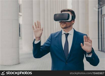 New cyberspace experience. Surprised male office worker dressed formally stands outdoors in 3d goggles and interacts with virtual interface, touching virtual objects, moving both hands in air. Surprised male office worker dressed formally stands outdoors in 3d goggles