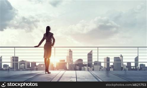 New day for business. Young elegant businesswoman on roof looking at city