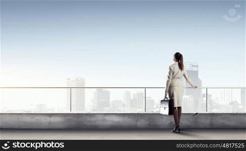 New day for business. Young elegant businesswoman on roof looking at city