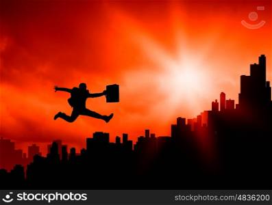 New day. Silhouette of jumping businessman over city in lights of sunrise
