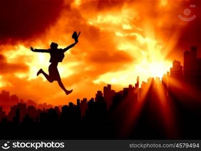 New day. Silhouette of jumping businesswoman over city in lights of sunrise