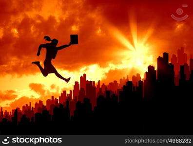 New day. Silhouette of jumping businesswoman over city in lights of sunrise