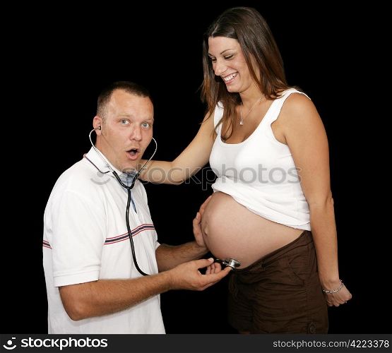 New father listening to his wife&rsquo;s pregnant belly with a stethescope. Black background