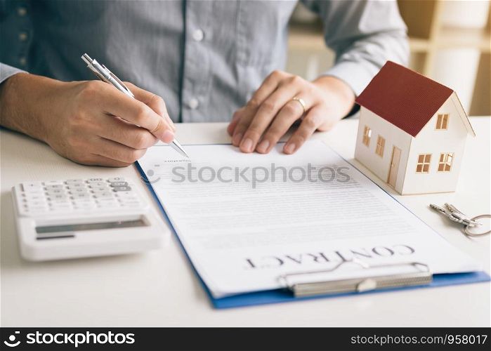 New home buyer signing contract on desk in office room.