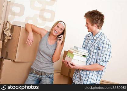 New house: Young couple with box in new home unpacking book, woman with mobile phone