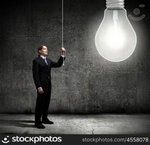 New idea. Young businessman and big light bulb against cement wall
