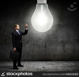 New idea. Young businessman and big light bulb against cement wall