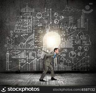 New idea. Young businessman carrying big light bulb on back