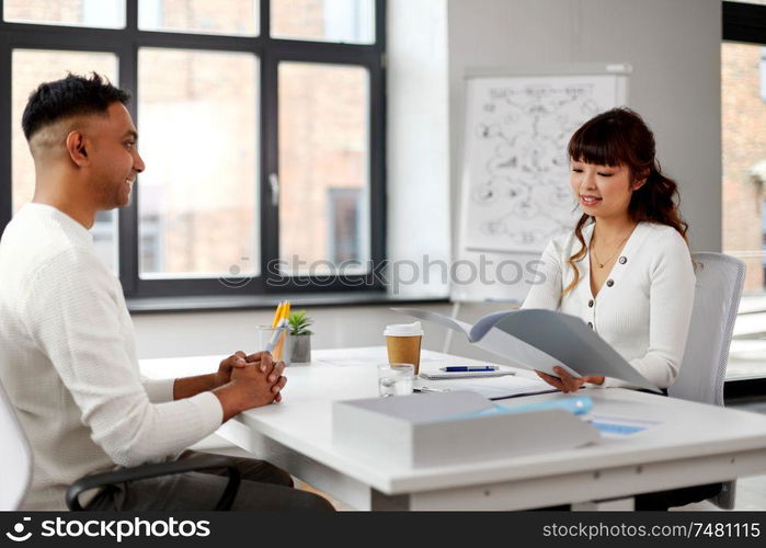 new job, business and employment concept - smiling asian female employer or hr manager with folder having interview with indian male employee at office. employer having interview with employee at office