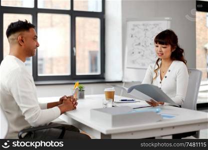 new job, business and employment concept - smiling asian female employer or hr manager with folder having interview with indian male employee at office. employer having interview with employee at office