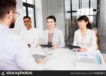 new job, hiring and employment concept - international team of recruiters with tablet computers having interview with male employee at office. recruiters having job interview with employee
