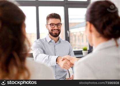 new job, hiring and employment concept - team of recruiters having interview with male employee and shaking hands at office. recruiters having job interview with male employee