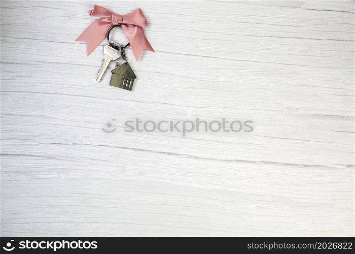 New keys of a house silver with keychain of little house top view with copy space and white wooden background, space for text. New keys of a house silver with keychain of little house top view with copy space and white wooden background,