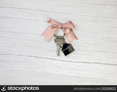 New keys of a house silver with keychain of little house top view with copy space and white wooden background, space for text. New keys of a house silver with keychain of little house top view with copy space and white wooden background,