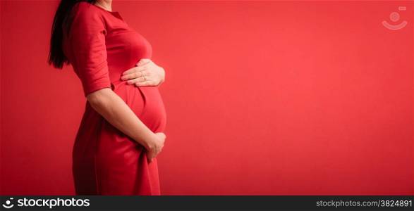 New life concept. Pregnancy, motherhood and happiness. Closeup on tummy of pregnant woman wearing stylish elegant red dress indoor
