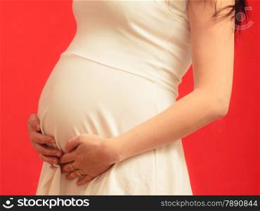 New life concept. Pregnancy, motherhood and happiness. Closeup on tummy of pregnant woman wearing stylish elegant white dress on red