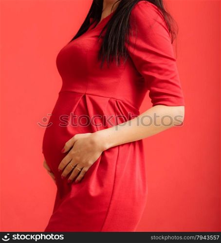 New life concept. Pregnancy, motherhood and happiness. Closeup on tummy of pregnant woman wearing stylish elegant red dress indoor