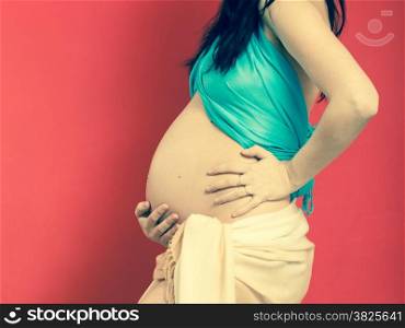 New life concept. Pregnancy, motherhood and happiness. Closeup tummy of pregnant woman wearing blue scarf on red