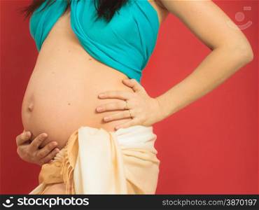 New life concept. Pregnancy, motherhood and happiness. Closeup tummy of pregnant woman wearing blue scarf on red