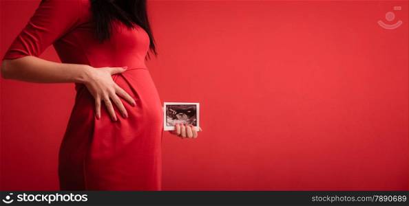 New life concept. Pregnancy, motherhood and happiness. Closeup tummy of pregnant woman wearing elegant red dress, ultrasound scan in hand indoor