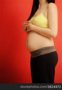 New life concept. Pregnancy, motherhood and happiness. Closeup tummy of pregnant woman on red