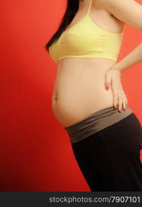 New life concept. Pregnancy, motherhood and happiness. Closeup tummy of pregnant woman on red