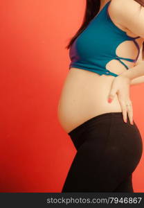 New life concept. Pregnancy, motherhood and happiness. Closeup tummy of pregnant woman on red